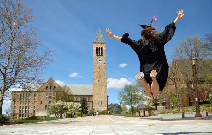 Student in cap and gown jumping with McGraw Clock Tower in the background